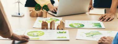 Wooden block represented green city and wind mill represented renewable energy was placed at center of green business meeting table with environmental document. Green business concept. Delineation. clipart