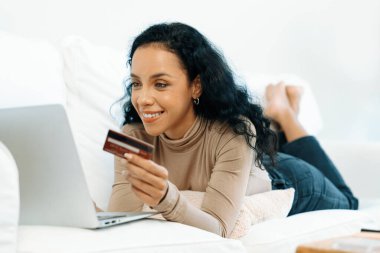 Genç mutlu bir kadın internetten alışveriş yaparak ürün satın alırken aynı zamanda internet üzerinden online kredi kartı ödeme sistemi ile çevrimiçi mağaza platformundan önemli siber güvenlik tarafından korunan ürünler sipariş ediyor.
