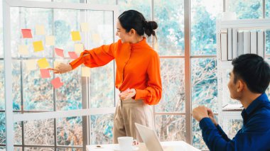 İş adamları ofisteki proje planlama kurulunda çalışıyor ve proje gelişimini analiz etmek için iş arkadaşlarıyla sohbet ediyorlar. Düzenli olması için cama yapıştırılmış yapışkan notlar kullanıyorlar. Jivy