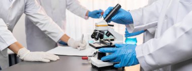 Kendini adamış bir grup bilim adamı yeni bir aşı ilacı ya da antibiyotik geliştirmek için tıbbi laboratuvarda mikroskop kullanarak kimyasal deney yapıyorlar. Biyoteknoloji laboratuvarı ve tıp araştırma konsepti. Neoterik