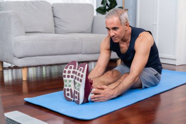 Aktif ve formda bir adam, evde egzersiz yapmadan önce ısınma ve esneme hareketleri yapıyor ve çevrimiçi fitness videosu izliyor. Emekliler için sağlıklı yaşam tarzı konsepti. Etki