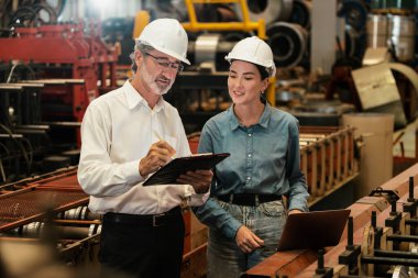Metal imalatında makine mühendisliği denetleyicisi olarak liderlik örneğini sunan çelik endüstriyel makineyi incelemek için dizüstü bilgisayar kullanan fabrika mühendisi ve asistan..