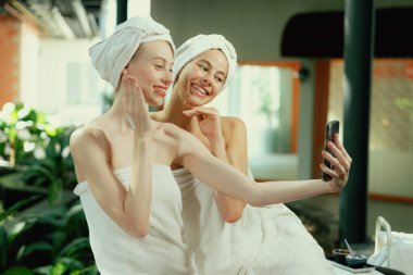 Beyaz havluyla güzel ciltli bir çift güzel kadın açık havada barışçıl doğal çevreyle çevrili bir şekilde fotoğraf çekiyorlar. Güzellik ve sağlıklı spa konsepti. Huzur.