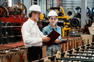Metal imalatında makine mühendisliği denetleyicisi olarak liderlik örneğini sunan çelik endüstriyel makineyi incelemek için dizüstü bilgisayar kullanan fabrika mühendisi ve asistan..