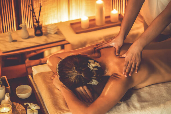 Caucasian woman customer enjoying relaxing anti-stress spa massage and pampering with beauty skin recreation leisure in warm candle lighting ambient salon spa at luxury resort or hotel. Quiescent