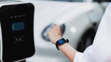 İş adamı, istasyonun otoparkından şarj olurken akıllı telefon hologramındaki EV aküsünün durumunu kontrol ediyor. EV teknolojisi adaptasyonu için temiz enerjinin gelecekteki yaşam tarzı. İnceleyin