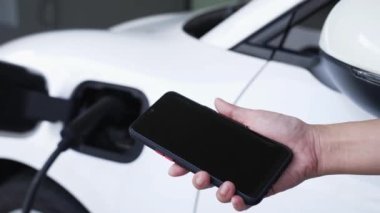 Akıllı telefon ekranı akıllı EV mobil uygulama üzerinde pil durumu EV araba garajdaki ev şarj istasyonu ile elektrik şarj ederken. Geleceğin yenilikçi EV arabası ve enerji sürdürülebilirliği. İnceleyin