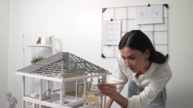 Genç, güzel ve zeki mühendisin yakın çekimleri modern ofiste duvarında taslak olan kalem kullanarak ev modelini ölçmeye odaklanıyor. Yaratıcı yaşam ve tasarım konsepti. Tertemiz..
