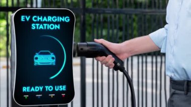 İşadamı EV şarj aletini şarj istasyonundan çıkarıp otoparktaki elektrikli arabayı şarj etmiş. CO2.Peruse 'u azaltmak için modern kentsel yaşam tarzı ve çevre dostu elektrikli araba kullanımı