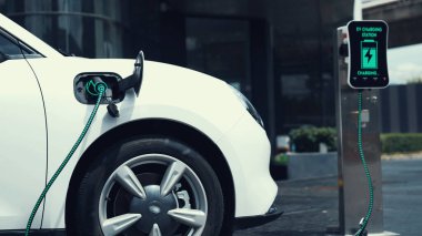 Şehir merkezinin otoparkındaki şarj istasyonuna bağlı elektrikli araba. Alternatif temiz ve sürdürülebilir enerji kullanan geleceğin yenilikçi yenilenebilir EV arabası. İnceleyin