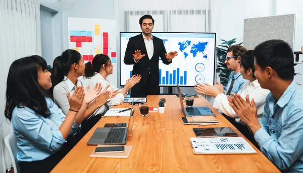 Group of happy multi ethnic businesspeople in celebratory gesture and successful teamwork after made success sales or positive financial data dashboard display on screen in meeting room. Habiliment