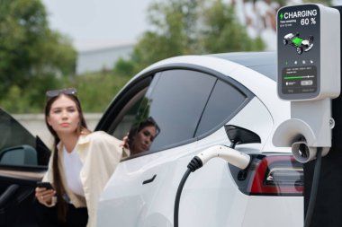 Genç bir kadın EV otomobil şarj istasyonu Green City Park 'ta elektrik ödemek için akıllı telefonu kullanıyor. Modern çevre ve EV araçlı sürdürülebilir şehir yaşam tarzı. Yararlı