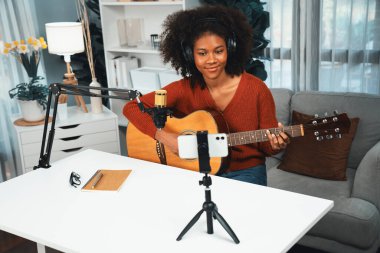 Genç Afrikalı Amerikalı müzisyenin sunucu kanalı gitar çalıyor, şarkı söylüyor, stüdyoda akıllı telefondan yayın yapıyor. Ekipman kulaklıkları dekorasyonu ve mikrofon kaydı. Tatlandırıcı.
