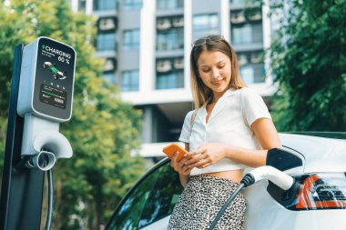 Genç bir kadın yazın yeşil sürdürülebilir şehir bahçesinde EV elektrikli arabasıyla seyahat ediyor. Kentsel sürdürülebilirlik yaşam tarzı yeşil temiz yeniden şarj edilebilir enerji elektrikli BEV araç iç organları