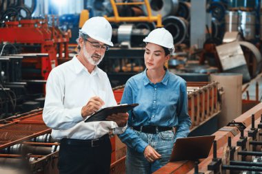 Metal imalatında makine mühendisliği denetleyicisi olarak liderlik örneğini sunan çelik endüstriyel makineyi incelemek için dizüstü bilgisayar kullanan fabrika mühendisi ve asistan..
