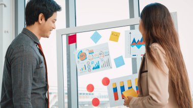 İş adamları ofisteki proje planlama kurulunda çalışıyor ve proje gelişimini analiz etmek için iş arkadaşlarıyla sohbet ediyorlar. Düzenli olması için cama yapıştırılmış yapışkan notlar kullanıyorlar. Jivy