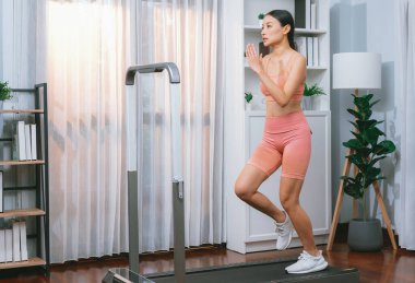 Enerjik ve güçlü atletik Asyalı kadın evde koşu makinası çalıştırıyor. Formda fiziğin takibi ve ev çalışması ve eğitimle sağlıklı yaşam tarzına bağlılık. Kuvvetli