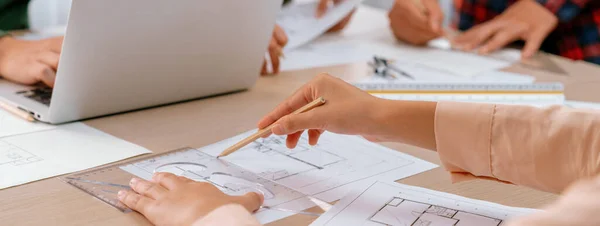 Professional architect drawing blueprint during meeting at modern architectural office on table with architectural document and stationary scatter around. Blurring background. Closeup. Delineation