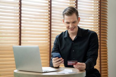 Genç adam internet bankacılığı için kredi kartlı dizüstü bilgisayar kullanıyor. İnternet üzerinden alışveriş yapıyor. Banka kartıyla modern ve kullanışlı online satın alma. Açılıyor