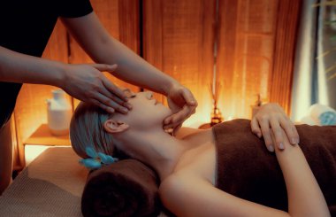 Beyaz kadın stres önleyici kafa masajı yapmaktan ve lüks otel veya otelde sıcak mum ışığında yüz güzelliği eğlencesi yapmaktan zevk alıyor. Sessiz.