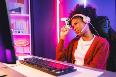 Afro-Amerikalı kız flaması, neon odada kulaklık takarak Esport yetenekli takımıyla online dövüş yaparken hayal kırıklığına uğradı. Rakiplerini kazanmak için strateji planlayan diğer oyuncularla konuşmak. Tatlandırıcı.