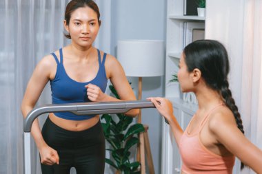 Enerjik ve güçlü atletik Asyalı kadın evde spor arkadaşı ya da antrenörü ile birlikte eliptik koşu makinesiyle koşuyor. Formda fiziğin takibi ve sağlıklı yaşam tarzına bağlılık. Kuvvetli