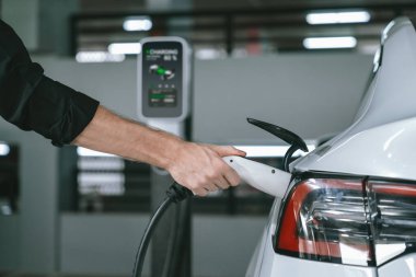 Genç adam EV elektrikli arabasıyla alışveriş merkezinin otoparkına gidiyor şehir merkezindeki şarj oluyor yeşil, temiz, yeniden şarj edilebilir elektrikli araç iç organları ile kentsel sürdürülebilirlik yaşam tarzını gösteriyor