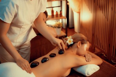 Lüks tatil köyündeki kaplıcalarda sıcak taş masajı, sıcak mum ışığı, spa bazalt taşı masajının keyfini çıkaran mutlu kadın müşteriler, rahatlatıcı bir sıcaklıkla vücudun üzerinde süzülüyorlar. Sessiz.