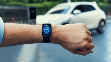 İş adamı, istasyonun otoparkından şarj olurken akıllı ekranda EV akü durumunu kontrol ediyor. EV teknolojisi adaptasyonu için temiz enerjinin gelecekteki yaşam tarzı. İnceleyin