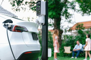 Evde şarj edilen elektrikli araba şarjını mutlu ve neşeli bir ailenin arka planına odakla. EV arabası daha iyi bir gelecek için alternatif ve sürdürülebilir enerji kullanıyor.