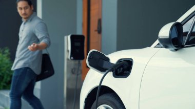 Adamın biri evinde elektrikli araç şarj aletinin fişini çekiyor. İlerici bir yaşam tarzında elektrikli araçların kullanımı, temiz ve sağlıklı bir çevreye katkıda bulunur..