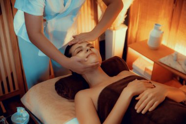 Beyaz kadın stres önleyici kafa masajı yapmaktan ve lüks otel veya otelde sıcak mum ışığında yüz güzelliği eğlencesi yapmaktan zevk alıyor. Sessiz.