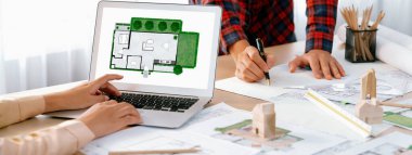 Profesyonel mimar, modern ofise yerleştirilen ahşap blok, plan ve mimari belge ile karışık masa üzerinde proje yöneticisi olarak dizüstü bilgisayarda sergilenen ECO evini temsil ediyordu. Kapatın. Tanımlama.