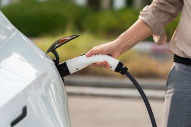 Genç adam, şehrin ticari otoparkındaki şarj istasyonundan elektrikli araba aküsünü şarj etmek için EV şarj aleti koymuş. Sürdürülebilir çevre dostu şehir yolculuğu için şarj edilebilir EV araba. Yararlı