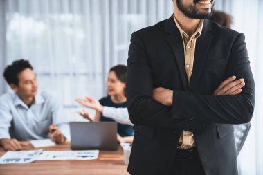 İş adamı, toplantı odasının arka planında çeşitli iş arkadaşlarıyla güven içinde poz veriyor. Çok kültürlü ekip iş başarısı için birlikte çalışır. Modern iş adamı portresi. Uyum