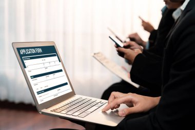 İş başvurusu yapan kişi diğer adaylarla iş görüşmesi için bekleme odasında otururken şirket şirketinde dizüstü bilgisayarla iş başvurusunda bulunuyor. Modern iş arayanlar ve iş arayanlar. Önde.