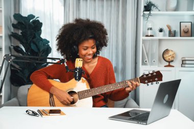 Genç Afrikalı Amerikalı müzisyenin sunucu kanalı gitar çalıyor, şarkı söylüyor, stüdyoda dizüstü bilgisayardan yayın yapıyor. Kulaklık dekorasyonu ve mikrofon kaydı. Tatlandırıcı.