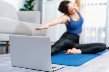 Çevrimiçi egzersiz videolarını gösteren yere odaklanmış dizüstü bilgisayar. Sportif atletik kadın ise arka planda ısınma ve esneme hareketleri üzerine yoğunlaşıyor. Kuvvetli