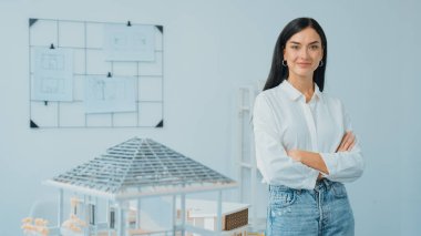 Genç, güzel, profesyonel mimar mühendisin portresini yakın plan ile birlikte beyaz modern ofiste ev modeliyle güven içinde pozlar veriyor. Yaratıcı yaşam ve tasarım. Tertemiz..