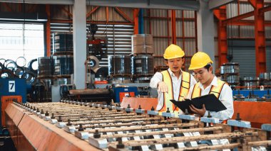 Ağır sanayi fabrikasındaki çelik üretim hattında endüstriyel malların optimal kalitede üretimi için mühendis tarafından denetlenirken fabrika işçisi metal damgalama makinesini çalıştırıyor. Örnek gösteriliyor