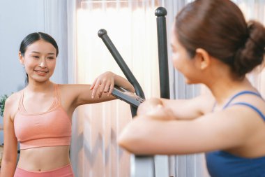 Enerjik ve güçlü atletik Asyalı kadın evde spor arkadaşı ya da antrenörü ile birlikte eliptik koşu makinesiyle koşuyor. Formda fiziğin takibi ve sağlıklı yaşam tarzına bağlılık. Kuvvetli