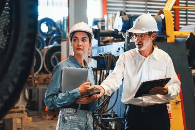 Metal imalatında makine mühendisliği denetleyicisi olarak liderlik örneğini sunan çelik endüstriyel makineyi incelemek için dizüstü bilgisayar kullanan fabrika mühendisi ve asistan..