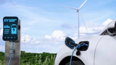Elektrikli araba, rüzgar türbini çiftliğinde çalışan akıllı EV şarj cihazıyla şarj edilen enerjiyi şarj ediyor. Alternatif temiz sürdürülebilir enerjinin teknolojik ilerlemesi. İnceleyin