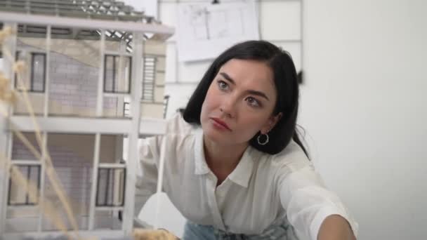 年轻漂亮的高加索建筑师工程师把房子模型转过来检查房子的结构 检查错误点 以解决现代办公室桌上的问题 穿上衣服纯洁无瑕 — 图库视频影像