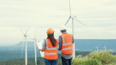 Erkek ve kadın mühendisler kırsal kesimdeki bir tepenin tepesinde ya da dağda rüzgar çiftliğinde çalışıyorlar. Yenilenebilir ve sürdürülebilir enerjinin gelecekteki üretimi için yenilikçi idealler.