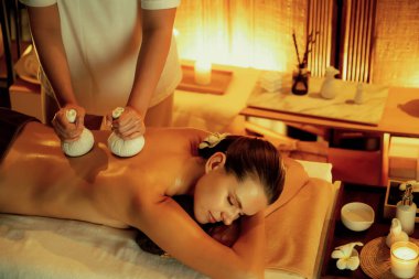 Sıcak bitkisel top spa masaj vücut tedavisi, masör kadın vücuduna nazikçe şifalı bitki torbası bastırıyor. Aromaterapi tesisinin sakinliği ve dinginliği kaplıca salonundaki mumların sıcacık ışığında. Sessiz.