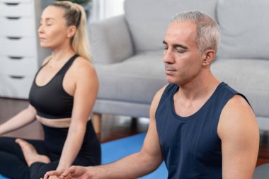 Spor giyim sektöründe aktif olan mutlu çift evde egzersiz paspası üzerinde meditasyon pozisyonunda yoga yapıyor. Huzurlu ve huzurlu bir huzur içinde sağlıklı bir emekli yaşam tarzı. Etki