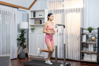 Enerjik ve güçlü atletik Asyalı kadın evde koşu makinası çalıştırıyor. Formda fiziğin takibi ve ev çalışması ve eğitimle sağlıklı yaşam tarzına bağlılık. Kuvvetli