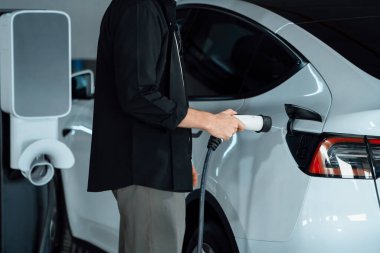 Genç adam EV elektrikli arabasıyla alışveriş merkezinin otoparkına gidiyor şehir merkezindeki şarj oluyor yeşil, temiz, yeniden şarj edilebilir elektrikli araç iç organları ile kentsel sürdürülebilirlik yaşam tarzını gösteriyor