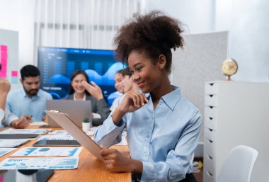 Bir grup ofis çalışanı ile birlikte arka planda ekranda gösterim paneliyle buluşan mutlu Afrikalı genç bir iş kadını portresi. Takım toplantısında kendine güveni tam bir ofis hanımı. Uyum